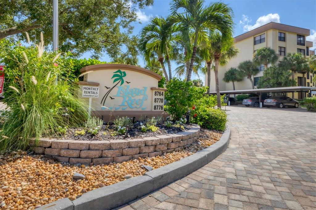 A stone sign for Island Reef stands at the entrance to a paved parking area — 8776 MIDNIGHT PASS ROAD UNIT C107, SARASOTA, FL