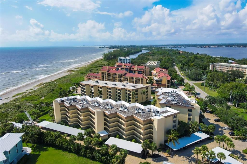 An aerial view shows multi-story apartment buildings situated along a sandy beach and coastline — 8776 MIDNIGHT PASS ROAD UNIT C107, SARASOTA, FL