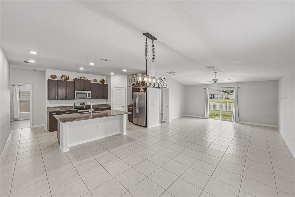 A kitchen with dark cabinets and a granite island opens into a large tiled living area — 4334 TROTTERS WAY, LAKELAND, FL