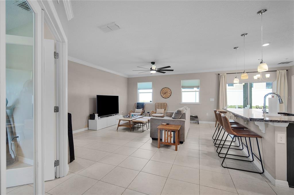 An open-concept living room and kitchen area featuring tile flooring, a ceiling fan, and barstools — 1328 WATER WILLOW DRIVE, GROVELAND, FL