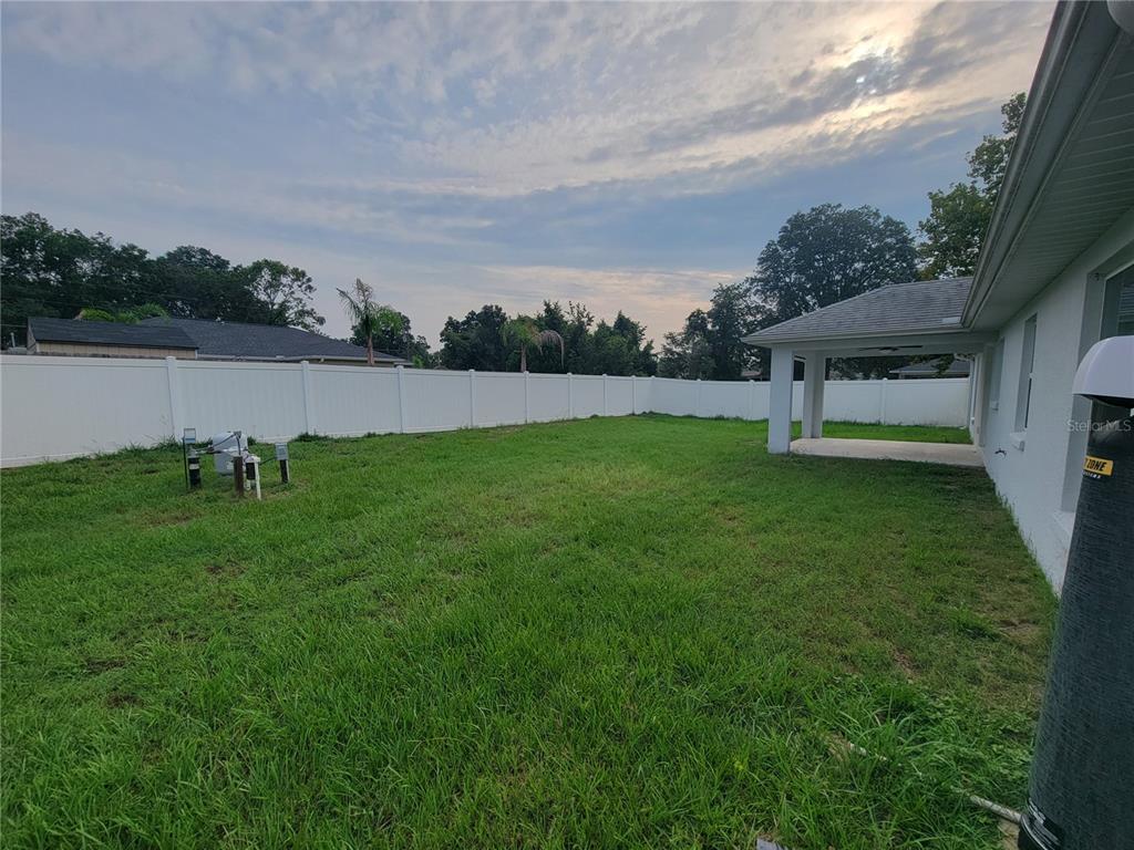 A grassy backyard features a white vinyl fence and a covered patio attached to a house — 8783 SE 157TH PLACE, SUMMERFIELD, FL