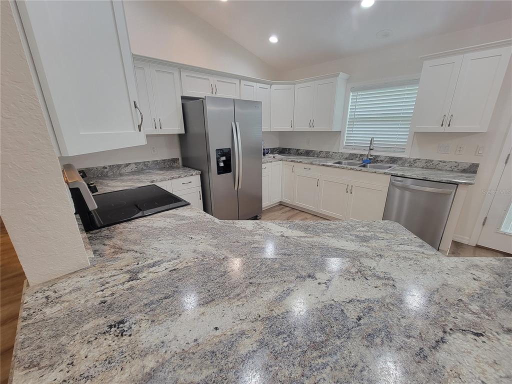 A kitchen features white cabinets, granite countertops, and stainless steel appliances — 8783 SE 157TH PLACE, SUMMERFIELD, FL
