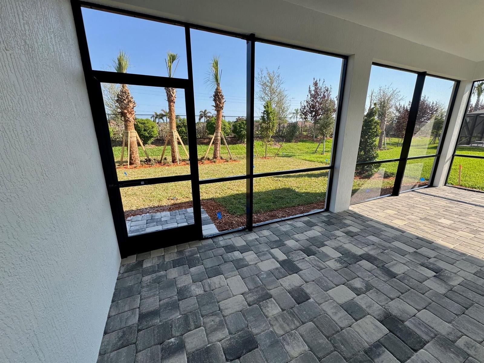 A screened-in patio with gray paver flooring overlooks a grassy backyard with young palm trees — 1205 Haven Circle # 30, Vero Beach FL 32960, VERO BEACH, FL