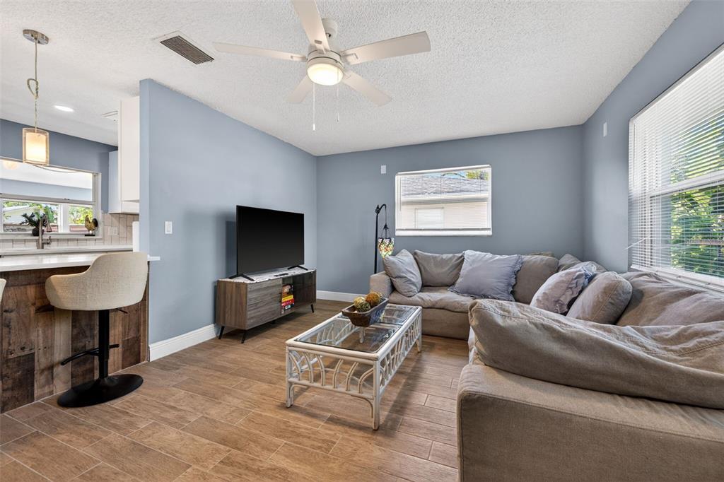 A living room features light blue walls, wood-look tile flooring, a sectional sofa, and television — 5810 VENETIAN BOULEVARD NE, ST PETERSBURG, FL