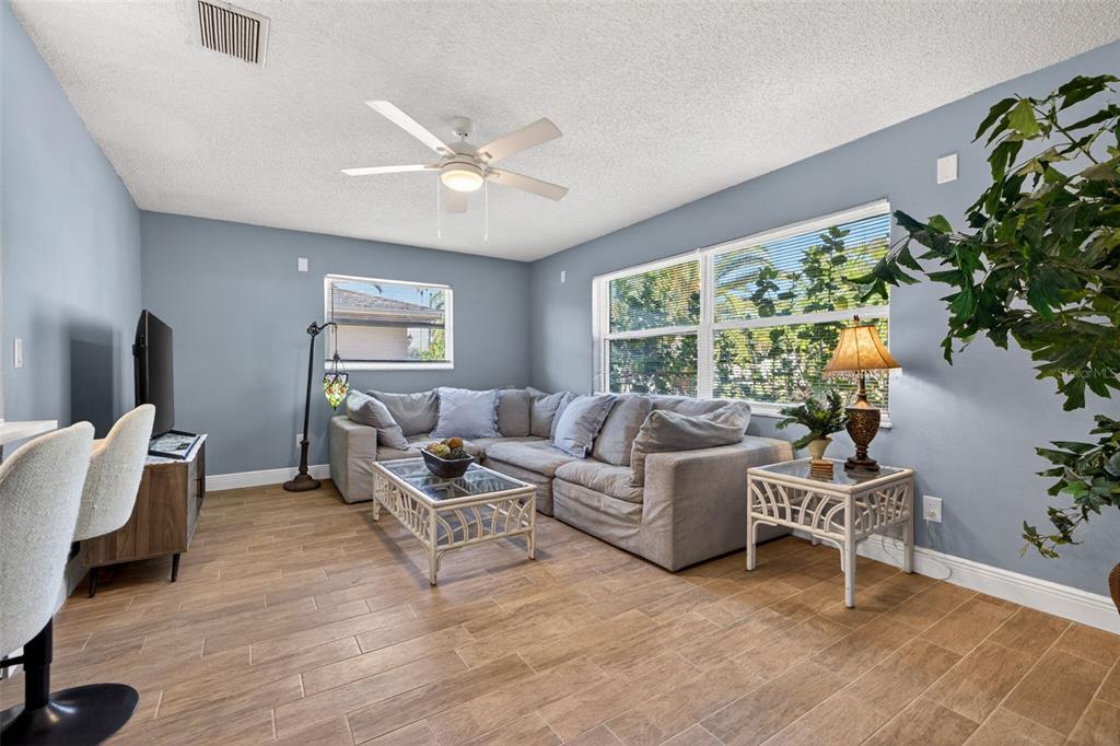 A living room with light blue walls, a gray sectional sofa, and wood-look tile flooring — 5810 VENETIAN BOULEVARD NE, ST PETERSBURG, FL