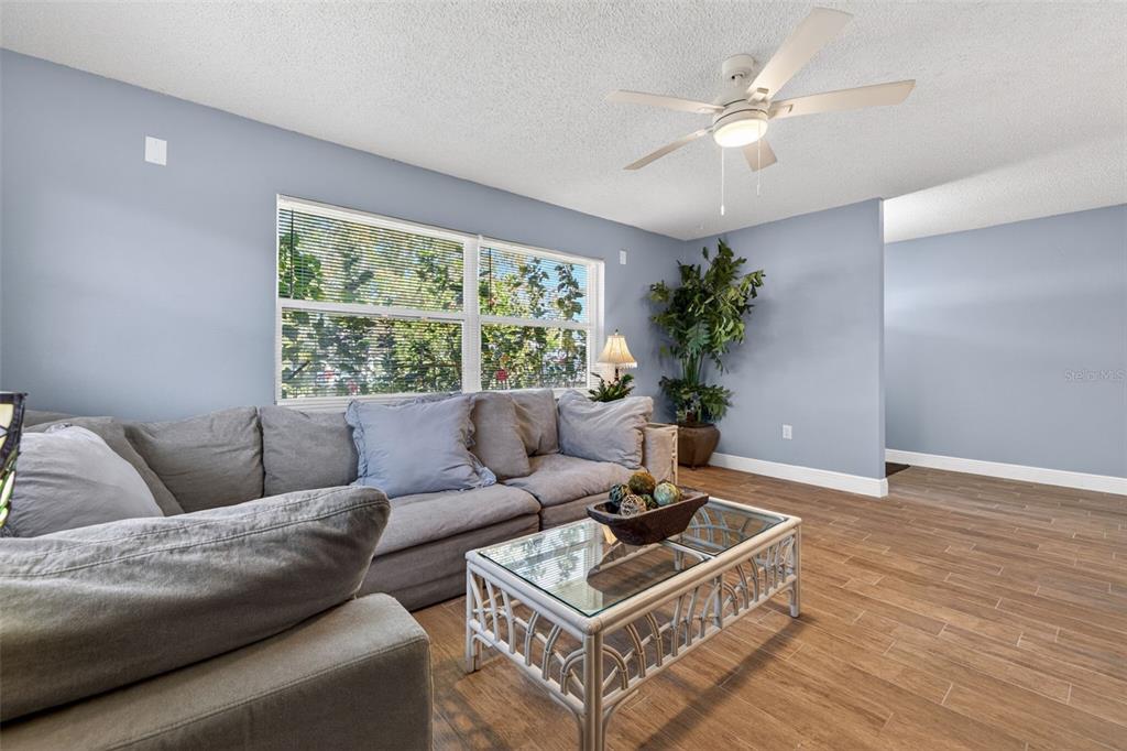 A living room features light blue walls, wood-look tile flooring, a gray sectional, and a ceiling fan — 5810 VENETIAN BOULEVARD NE, ST PETERSBURG, FL