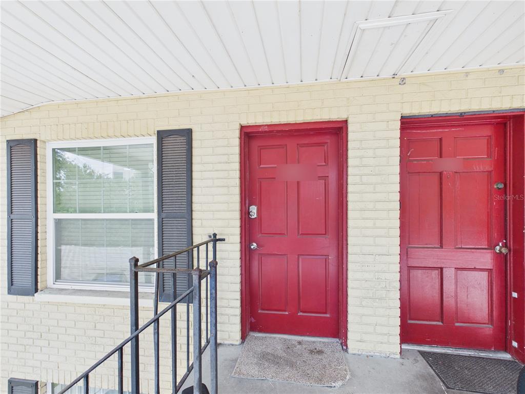 A yellow brick exterior wall features two red doors and a window with shutters — 2800 E 113TH AVENUE UNIT 219, TAMPA, FL