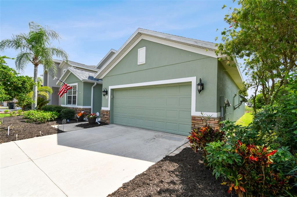 A green house with a two-car garage and a paved driveway under a blue sky — 5056 LAKEHURST COURT, PALMETTO, FL