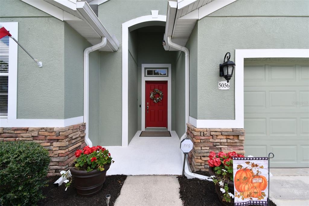The exterior of a house features a red front door, stone accents, and potted flowers — 5056 LAKEHURST COURT, PALMETTO, FL