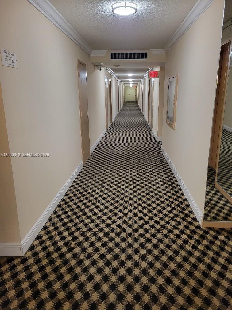 A long apartment building hallway features beige walls, a checkered carpet, and recessed ceiling lights — 1833 S Ocean Dr # 307, Hallandale Beach FL 33009, HALLANDALE BEACH, FL