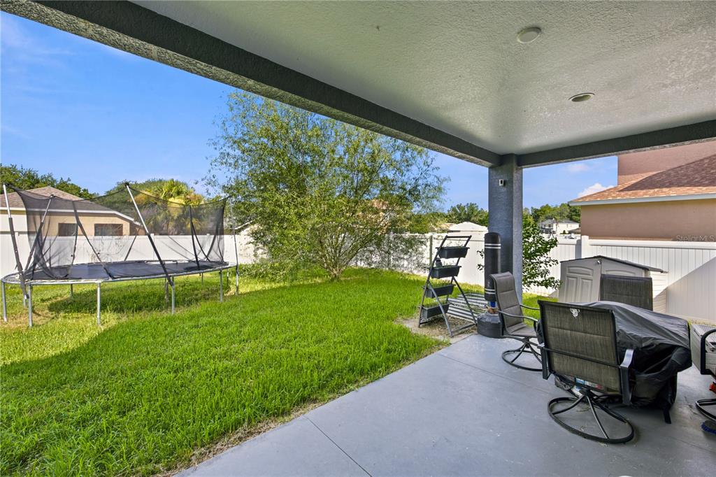 A covered concrete patio overlooks a backyard with a trampoline and a white vinyl fence — 3970 SW 51ST TERRACE, OCALA, FL