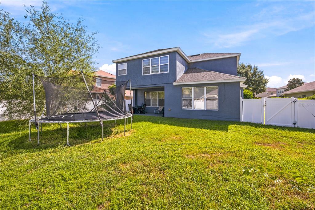 The backyard features a large trampoline, a blue two-story house, and a white privacy fence — 3970 SW 51ST TERRACE, OCALA, FL