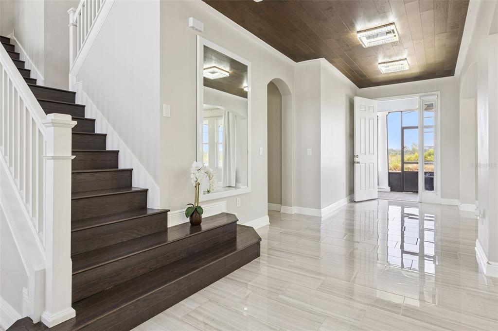 A foyer features a dark wood staircase, a large wall mirror, and a wood-paneled ceiling — 359 BLUE CYPRESS DRIVE, GROVELAND, FL