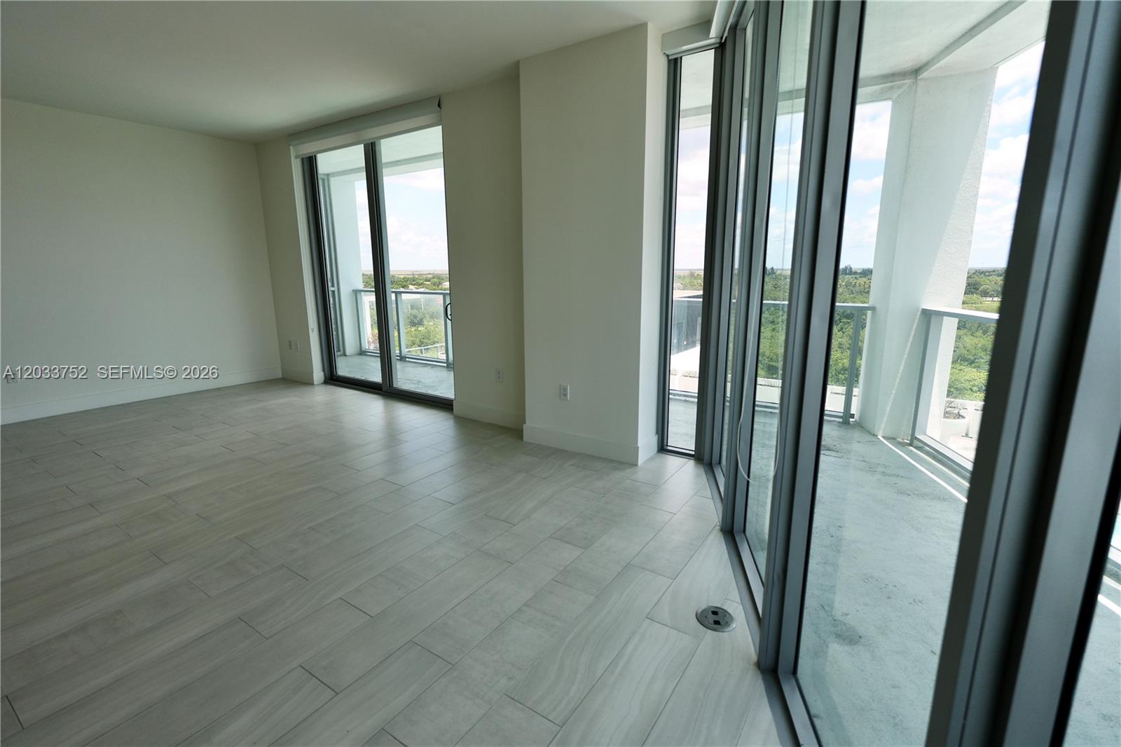 An empty room features light-colored tile flooring, white walls, and floor-to-ceiling glass sliding doors — 2000 Metropica Way # 810, Sunrise FL 33323, SUNRISE, FL