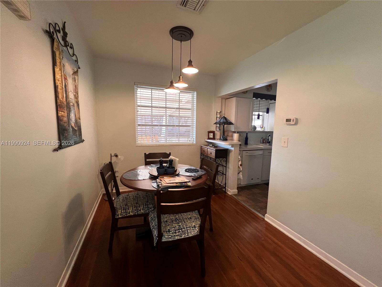 A dining area features a round wooden table, three chairs, and a hanging light fixture — 151 W 63rd St, Hialeah FL 33012, HIALEAH, FL