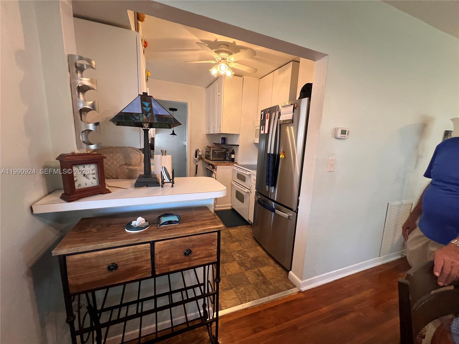 A kitchen with white cabinets and stainless steel appliances is viewed from an adjacent room — 151 W 63rd St, Hialeah FL 33012, HIALEAH, FL
