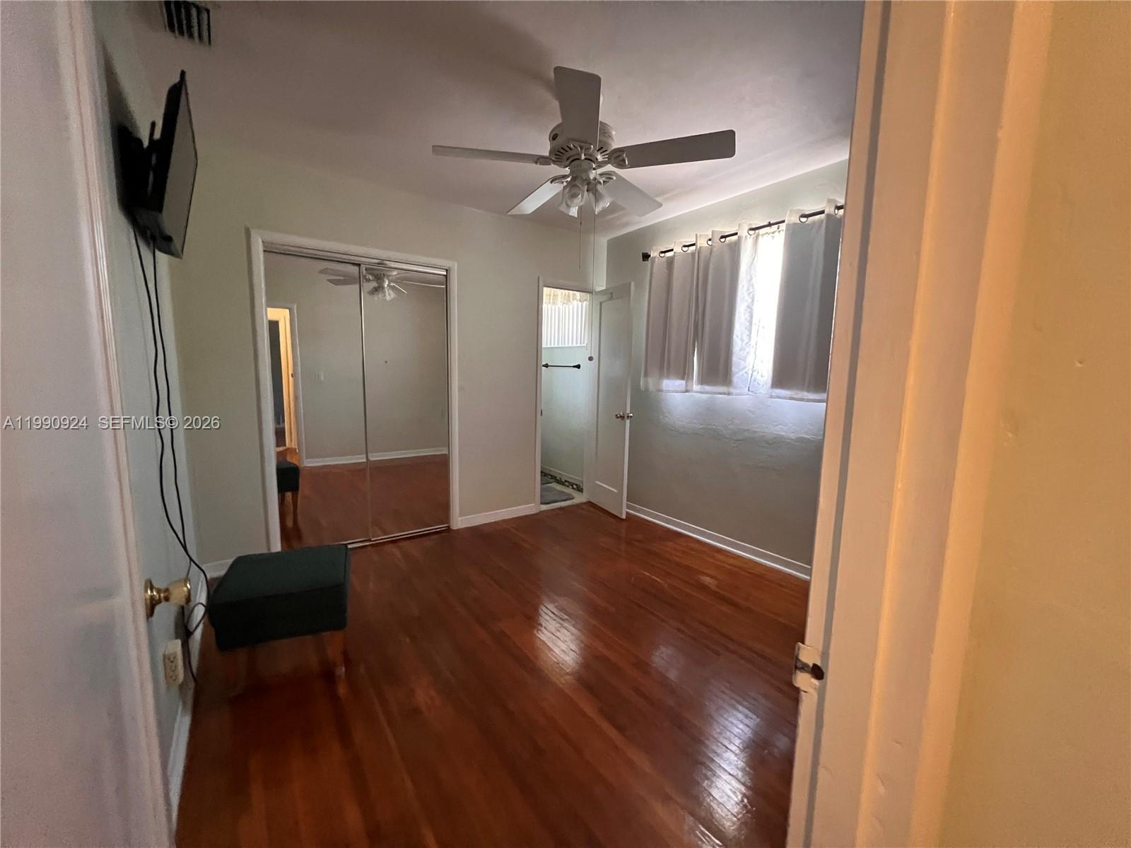 A bedroom features hardwood floors, a ceiling fan, mirrored closet doors, and a window — 151 W 63rd St, Hialeah FL 33012, HIALEAH, FL
