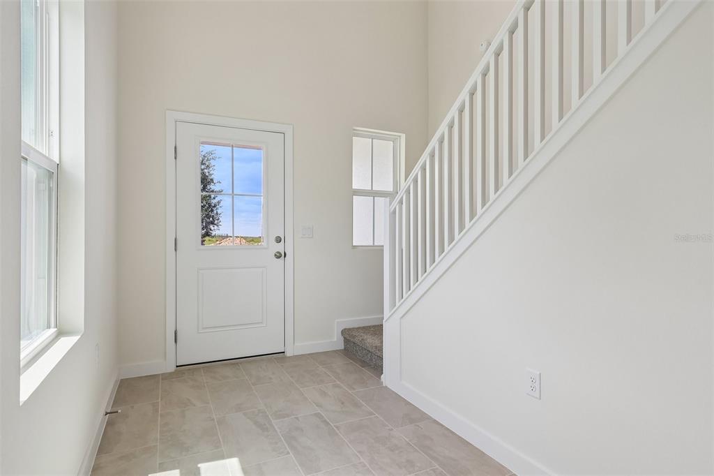 An entryway features tile flooring, a white front door, and a staircase with white railings — 1357 JUNE LAKE LOOP, HAINES CITY, FL