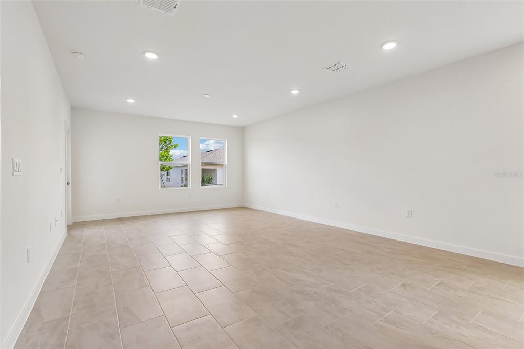 An empty room with light-colored tile flooring, white walls, recessed lighting, and two windows — 1357 JUNE LAKE LOOP, HAINES CITY, FL