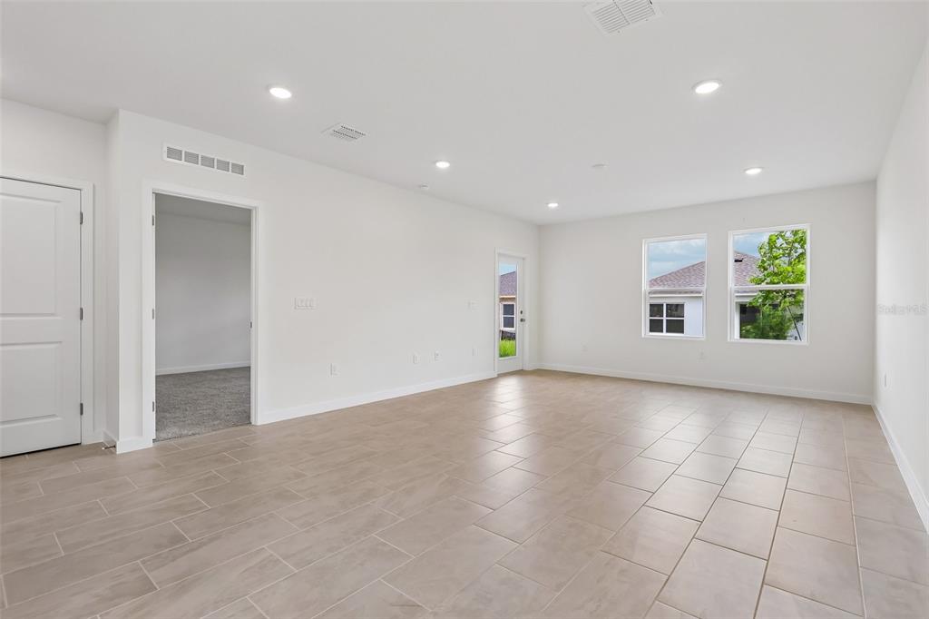 A spacious, empty room features light-colored tile flooring, white walls, recessed lighting, and two windows — 1357 JUNE LAKE LOOP, HAINES CITY, FL
