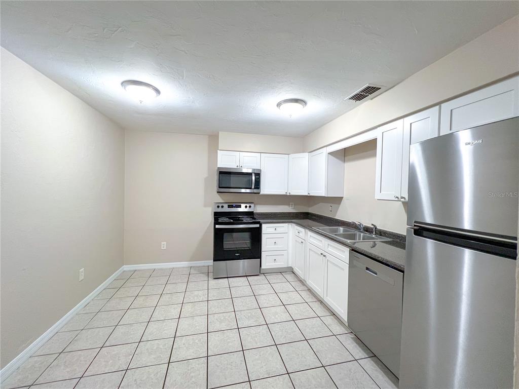 A kitchen features white cabinets, stainless steel appliances, dark countertops, and light-colored tile flooring — 703 SW 69TH TERRACE UNIT B, GAINESVILLE, FL