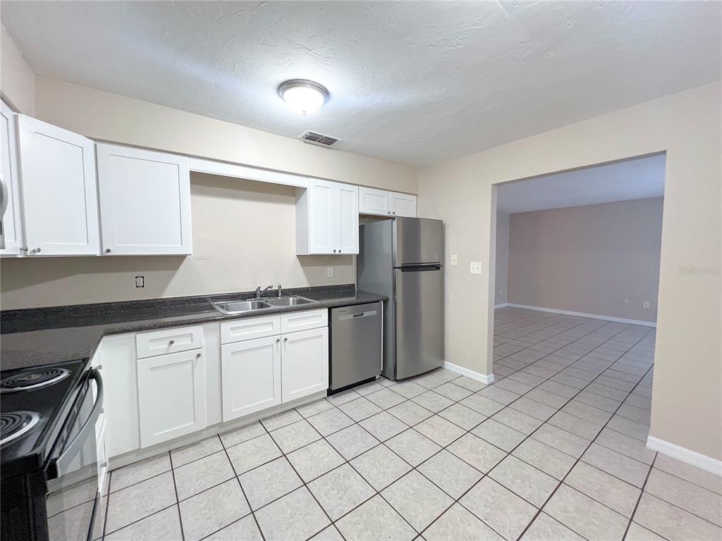 A kitchen features white cabinets, stainless steel appliances, dark countertops, and light-colored tiled flooring — 703 SW 69TH TERRACE UNIT B, GAINESVILLE, FL