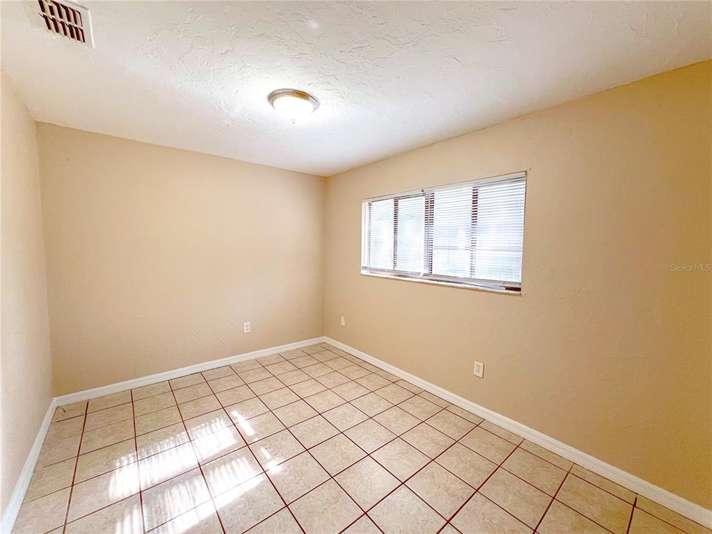 An empty room with beige walls, white trim, and light-colored tiled flooring — 703 SW 69TH TERRACE UNIT B, GAINESVILLE, FL