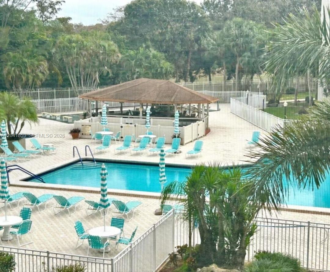 An elevated view of a swimming pool area with lounge chairs, umbrellas, and a gazebo — 3910 Inverrary Blvd # B, Lauderhill FL 33319, LAUDERHILL, FL