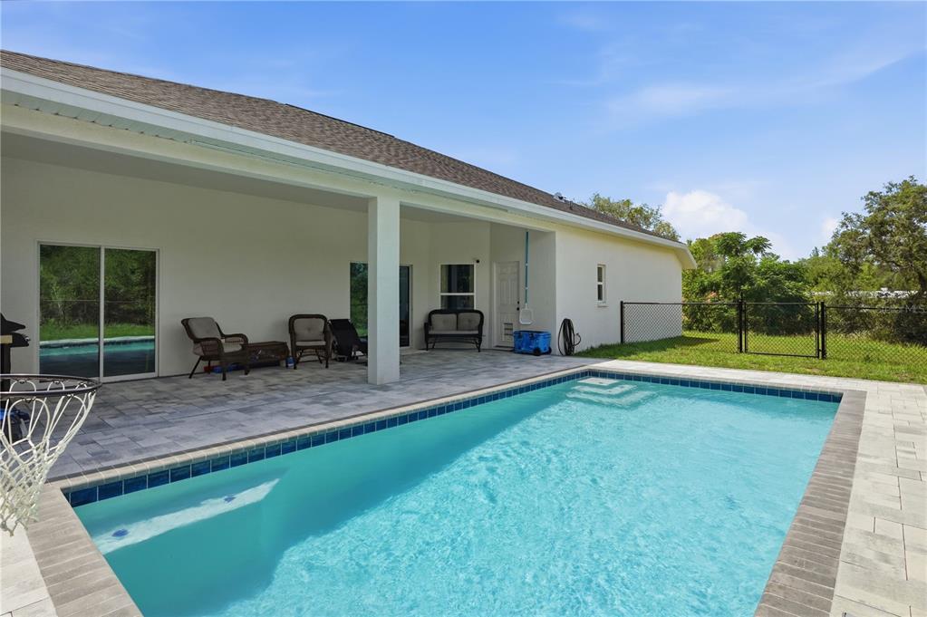 A swimming pool sits in front of a covered patio with a paved deck — 7279 BLACKBIRD AVENUE, WEEKI WACHEE, FL