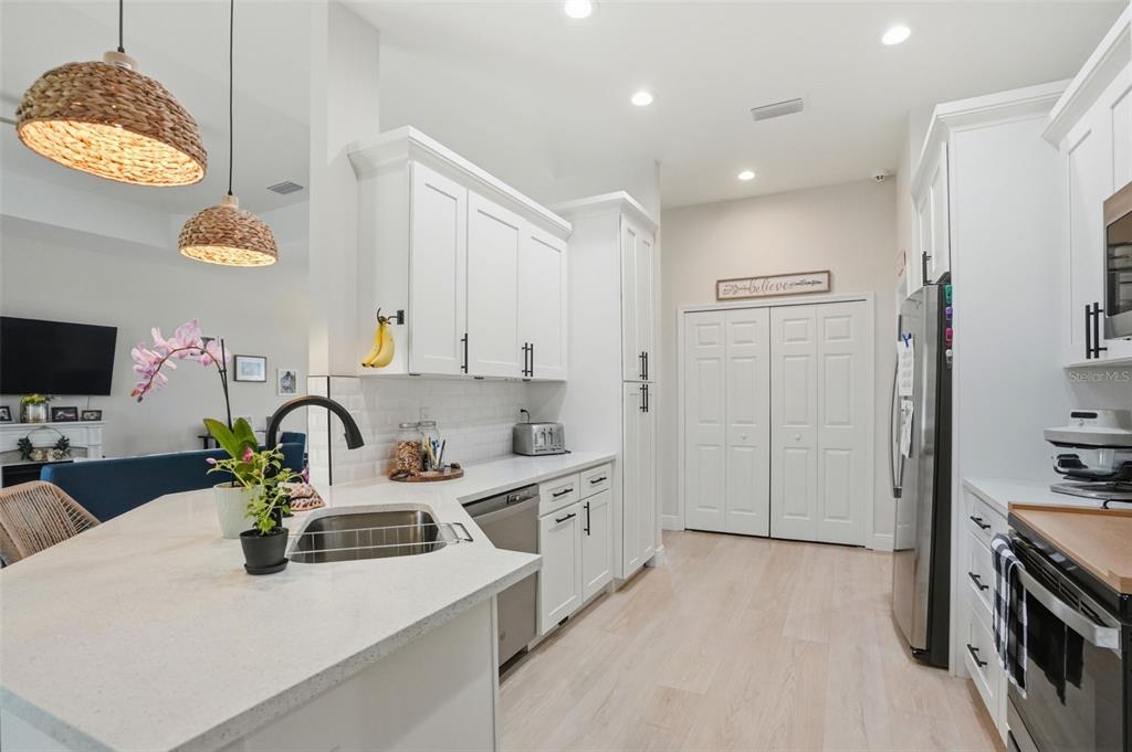 A bright kitchen features white cabinets, light countertops, stainless steel appliances, and two woven pendant lights — 7279 BLACKBIRD AVENUE, WEEKI WACHEE, FL