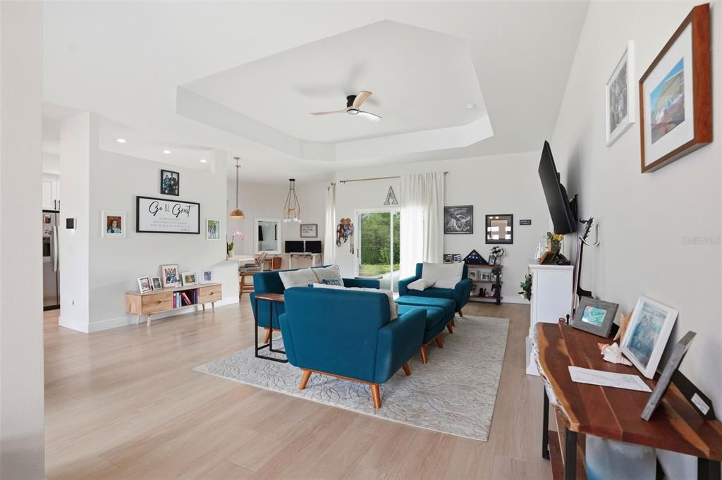A bright living room features a tray ceiling, light wood flooring, and blue upholstered furniture — 7279 BLACKBIRD AVENUE, WEEKI WACHEE, FL