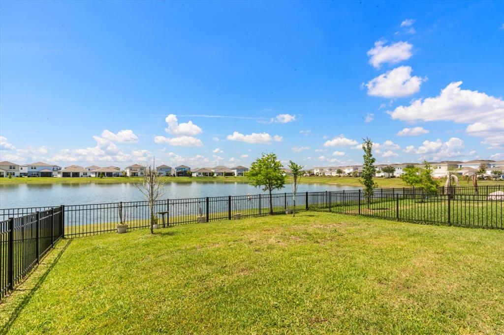 A fenced grassy backyard overlooks a large pond with a residential neighborhood in the distance — 2624 BLOWING BREEZE AVENUE, KISSIMMEE, FL