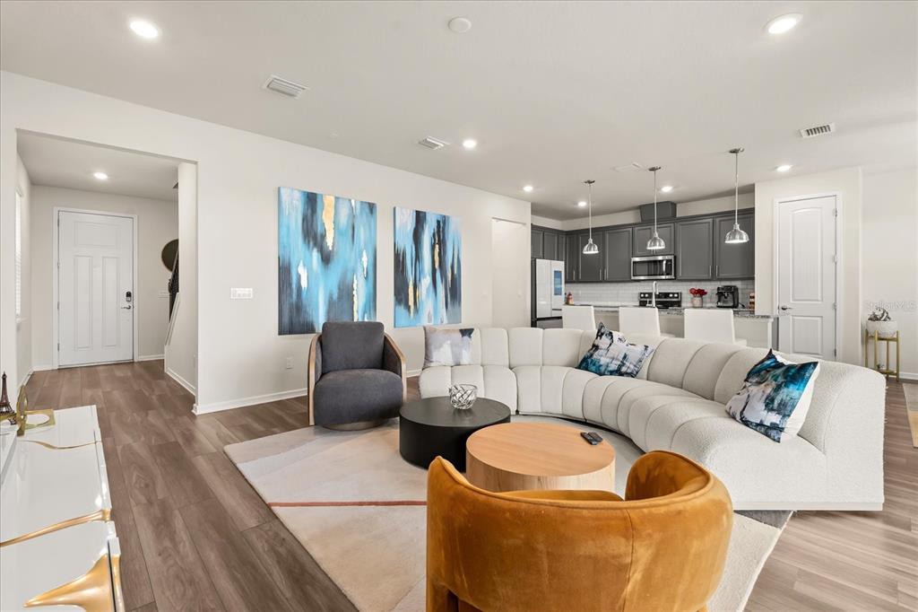 An open-concept living room features a curved white sofa, two accent chairs, and a kitchen — 2624 BLOWING BREEZE AVENUE, KISSIMMEE, FL