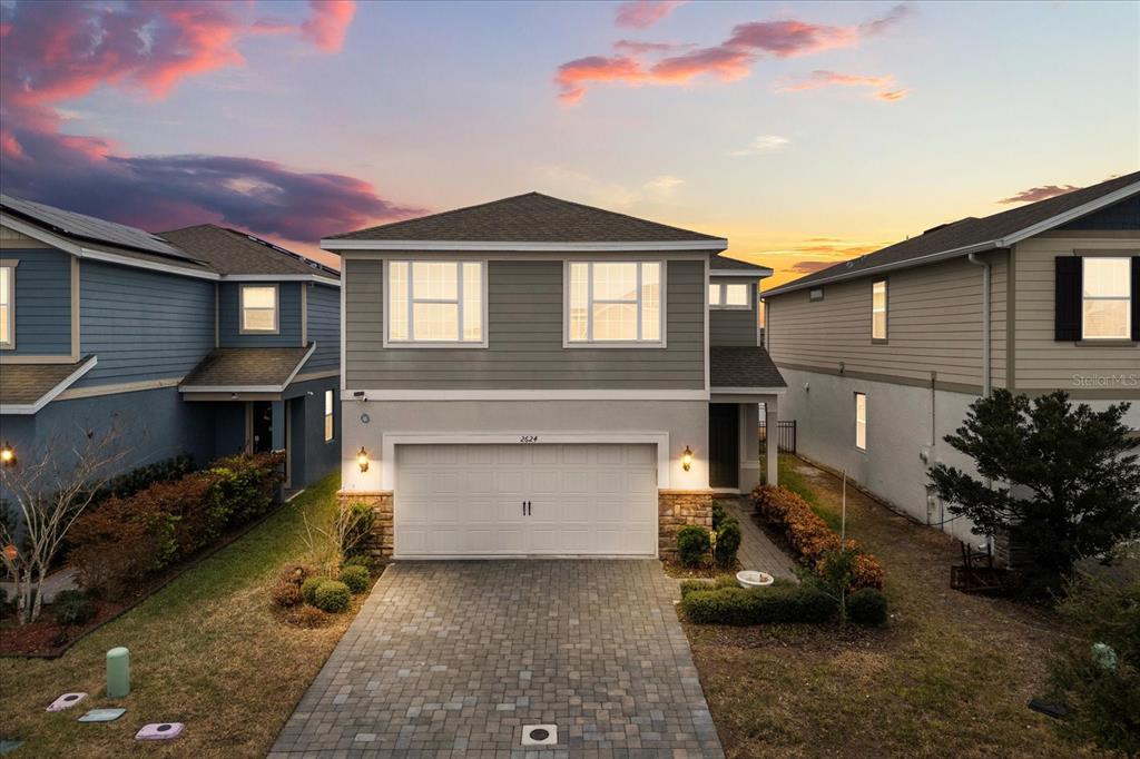 A two-story house with a paved driveway and a two-car garage at sunset — 2624 BLOWING BREEZE AVENUE, KISSIMMEE, FL