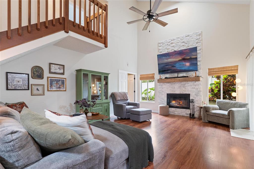 A living room features a stone fireplace, vaulted ceiling, wood flooring, and a wooden staircase — 3274 MONTROSE CIRCLE, PALM HARBOR, FL