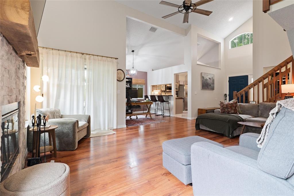 A living room with hardwood floors, a stone fireplace, and an open view to the kitchen — 3274 MONTROSE CIRCLE, PALM HARBOR, FL
