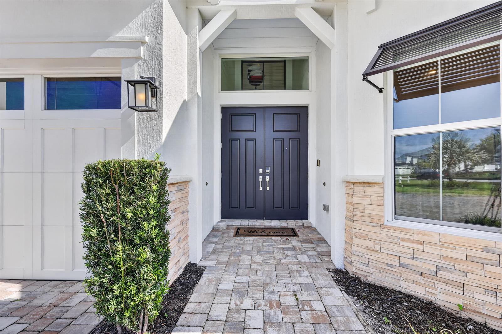 A paved walkway leads to a dark double front door under a white covered entryway — 20160 SE Bridgewater Drive, Jupiter FL 33458, JUPITER, FL