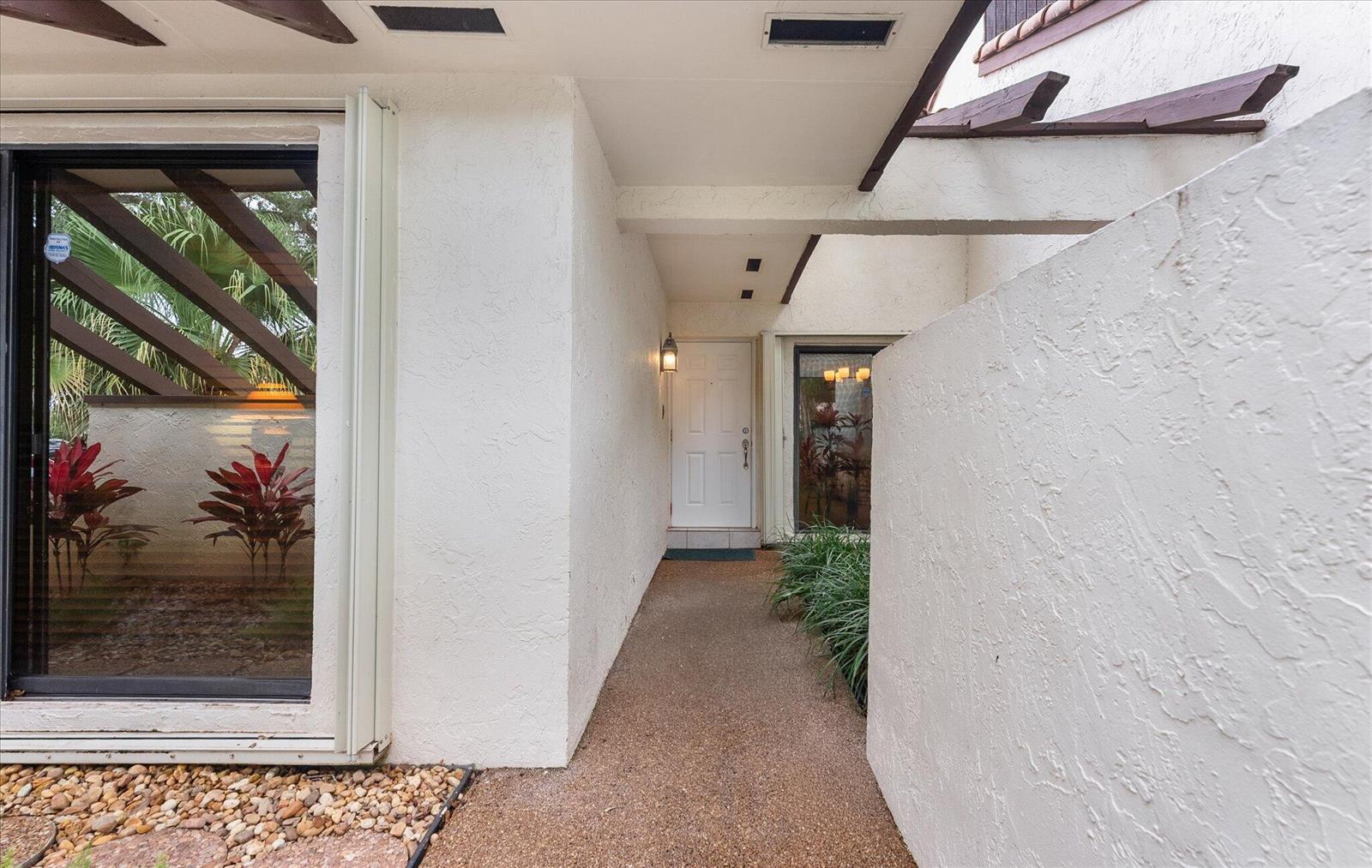 A white front door is accessed by a narrow, aggregate-paved walkway between two stucco walls — 6886 Tiburon Circle, Boca Raton FL 33433, BOCA RATON, FL