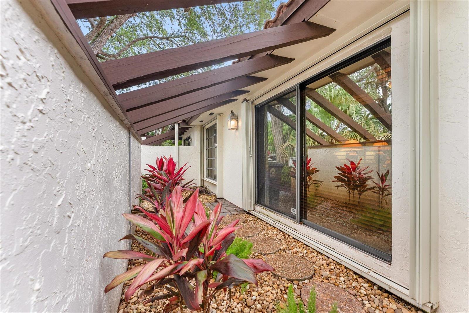 A narrow outdoor courtyard features a brown wooden pergola, gravel ground, and red-leafed plants — 6886 Tiburon Circle, Boca Raton FL 33433, BOCA RATON, FL
