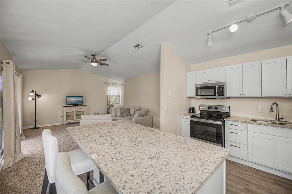 A living room with beige walls, carpeted flooring, a ceiling fan, and a sliding glass door — 14415 WORTHWHILE ROAD, PORT CHARLOTTE, FL