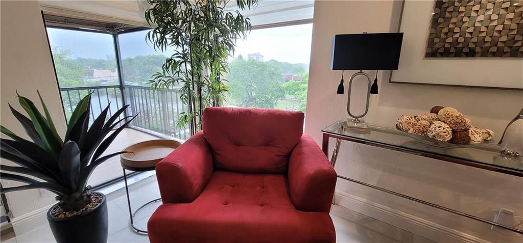 A red armchair sits in a room with a glass console table and balcony view — 6010 S Falls Circle Drive # 423, Lauderhill FL 33319, LAUDERHILL, FL