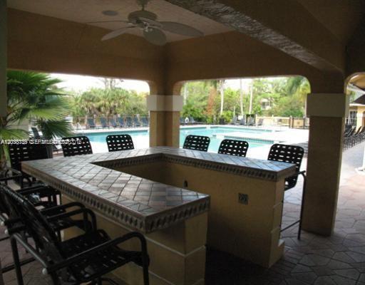 An outdoor covered bar with tiled countertops and metal chairs overlooks a swimming pool — POMPANO BEACH, FL
