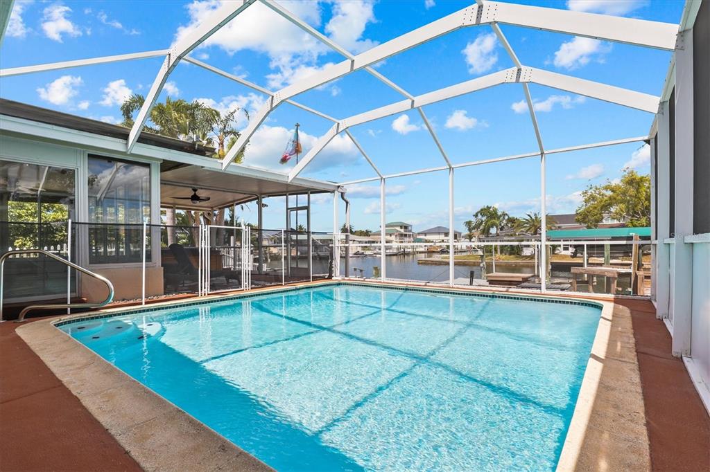 A swimming pool sits inside a screened-in lanai overlooking a canal with boat docks — 7239 SOUTHWIND DRIVE, HUDSON, FL