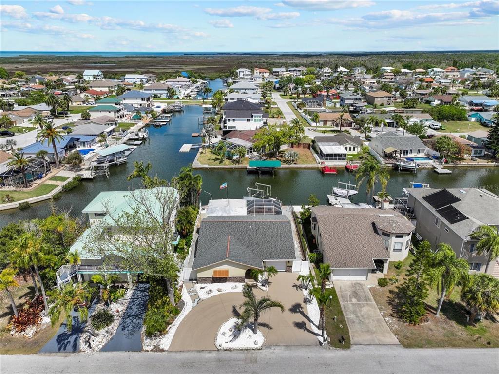 An aerial view shows a residential neighborhood with houses along a canal leading to water — 7239 SOUTHWIND DRIVE, HUDSON, FL