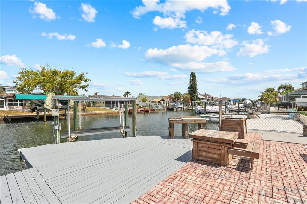 A gray wooden dock and brick patio overlook a canal with boat lifts and houses — 7239 SOUTHWIND DRIVE, HUDSON, FL