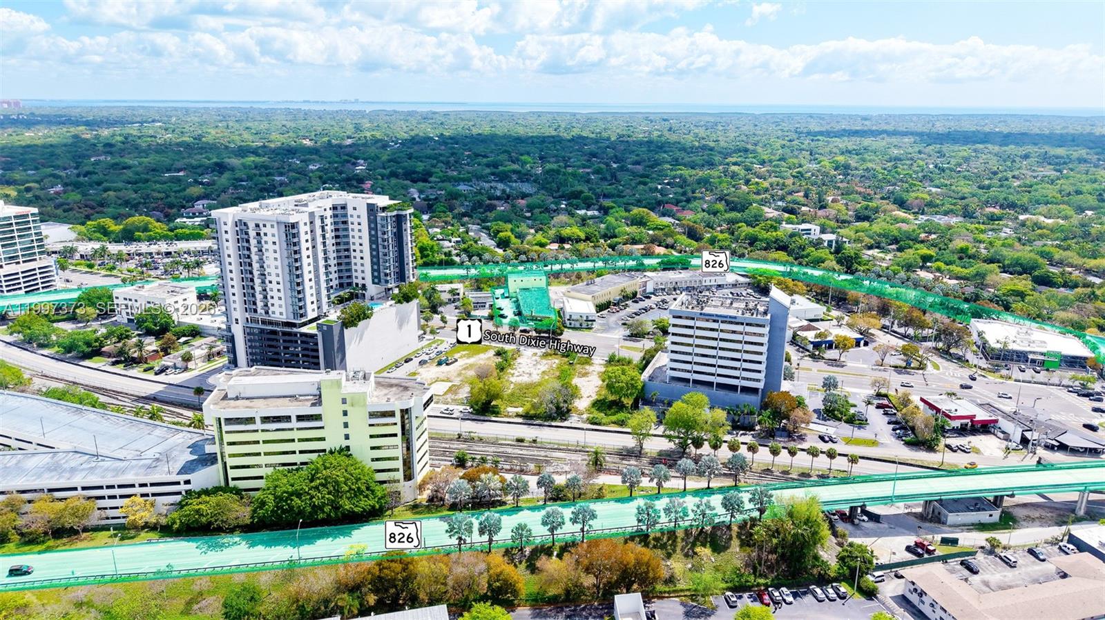 An aerial view shows high-rise buildings, a highway, and surrounding greenery in a suburban area — 9621 S Dixie Hwy, Pinecrest FL 33156, PINECREST, FL
