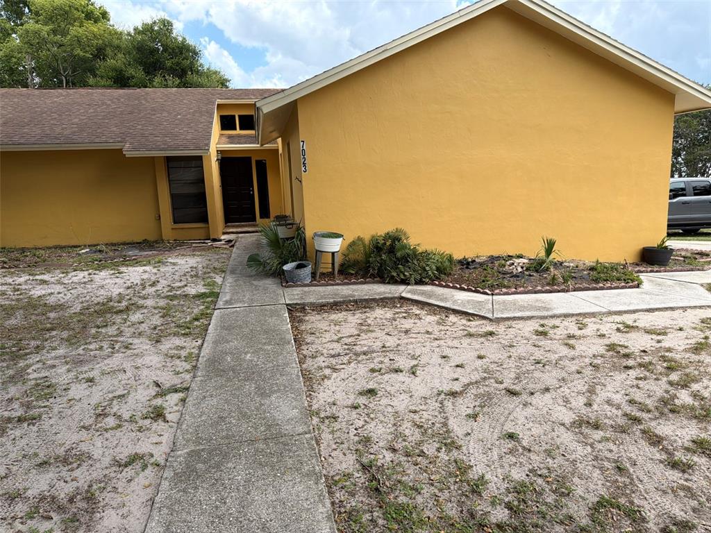 A yellow house with a brown roof and a concrete walkway leading to the entrance — 7023 FOX CHASE DRIVE, LAKELAND, FL