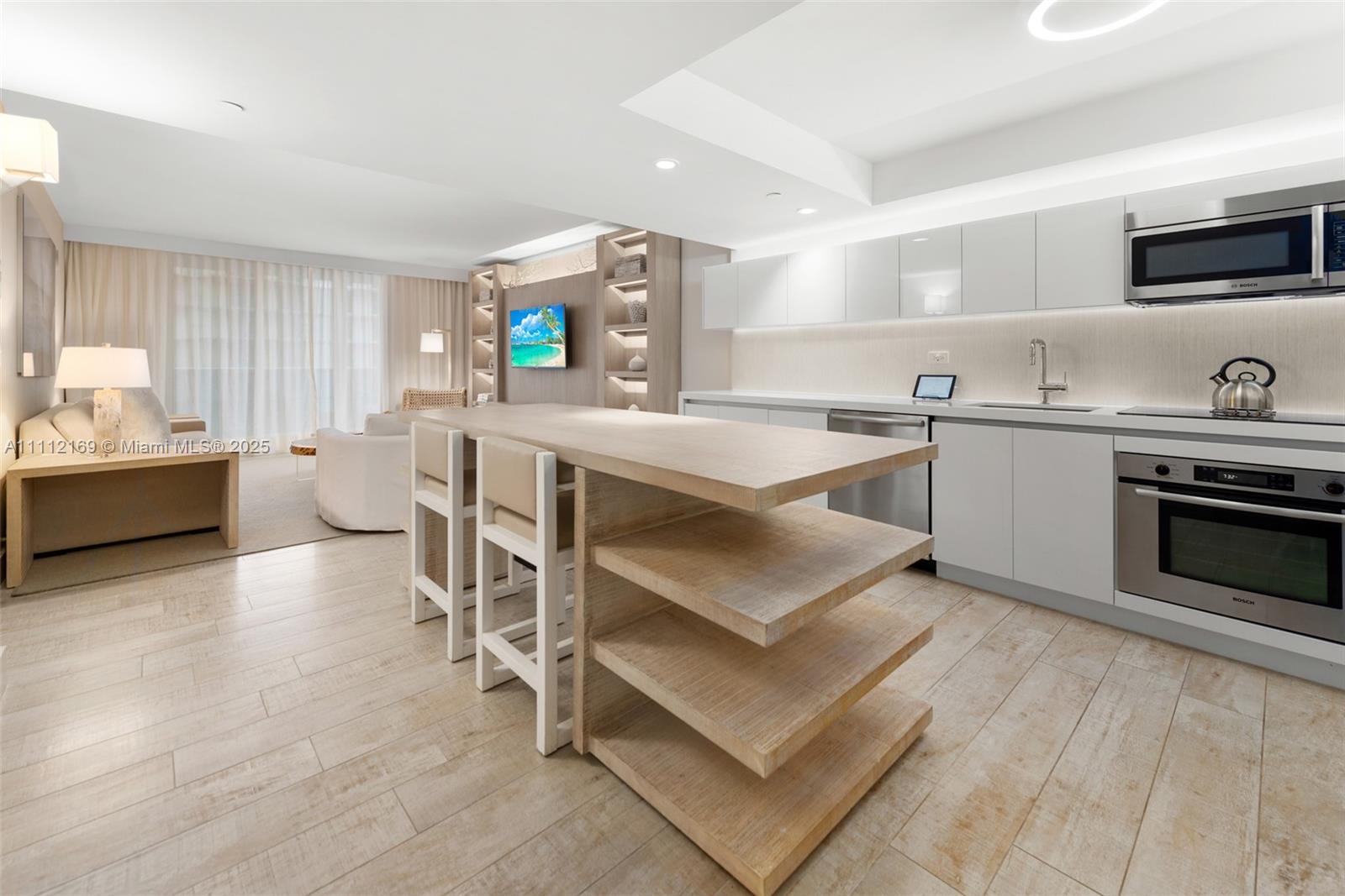 A modern kitchen with light wood cabinetry and an island sits beside a living area — 102 24th St # 1211, Miami Beach FL 33139, MIAMI BEACH, FL