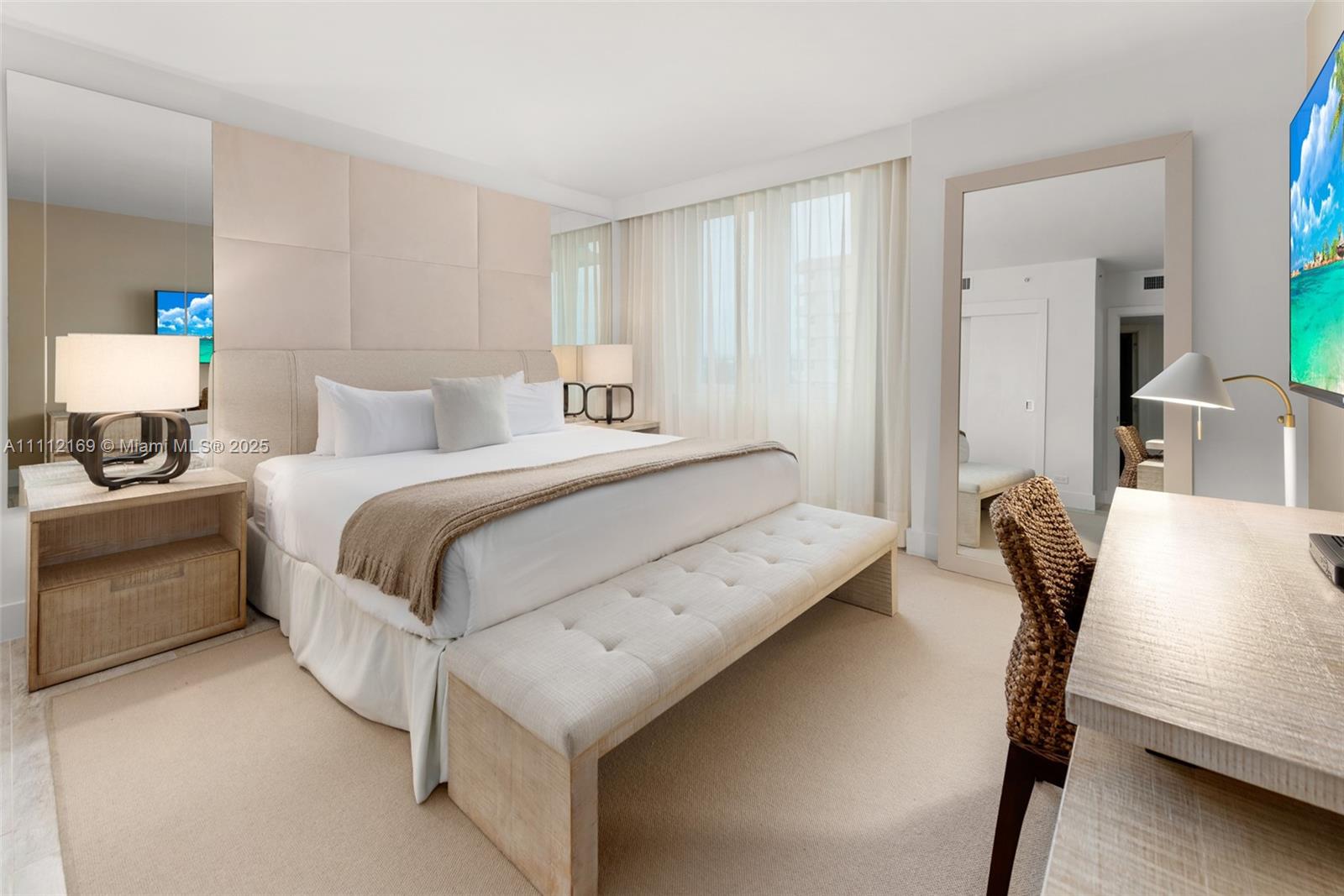 A bedroom features a king bed, tufted bench, desk, and large mirror with neutral decor — 102 24th St # 1211, Miami Beach FL 33139, MIAMI BEACH, FL