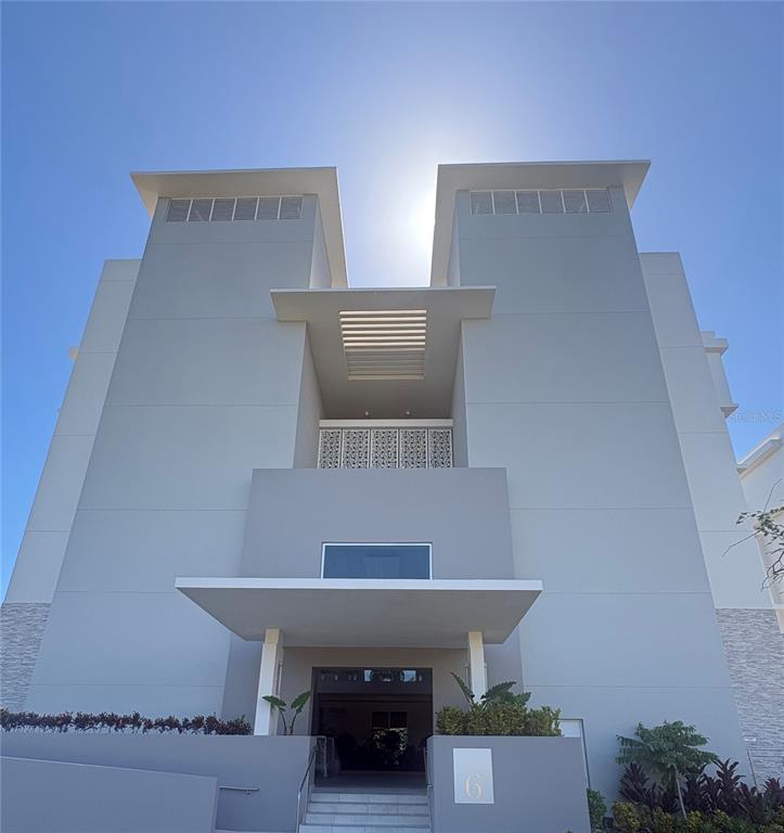 A low-angle exterior view of a modern, multi-story building with a central entrance and balcony — Ocean Drive FOUR SEASONS PRIVATE RESIDENCES UNIT 6401, RIO GRANDE, PR